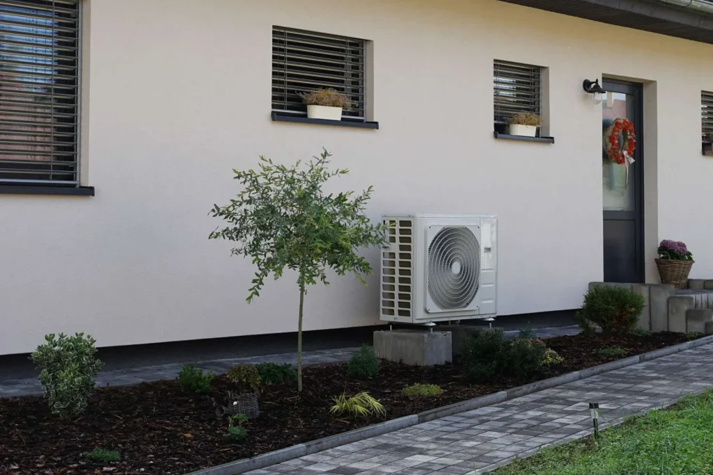 Unité extérieure d'une pompe à chaleur installée sur le mur d'une maison moderne avec un petit jardin paysager.